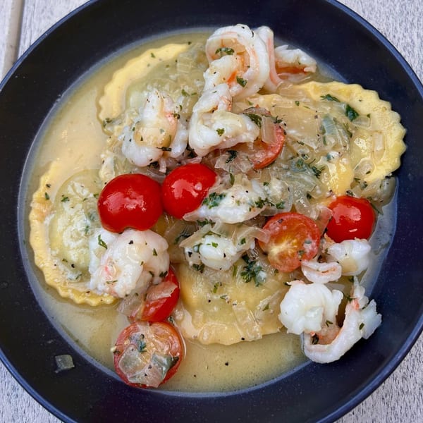 Ravioli with shrimp, cherry tomatoes, and onions in a creamy sauce, garnished with herbs.