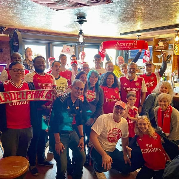 A large group of smiling people in red Arsenal jerseys and scarves pose inside Trooper Thorn's.