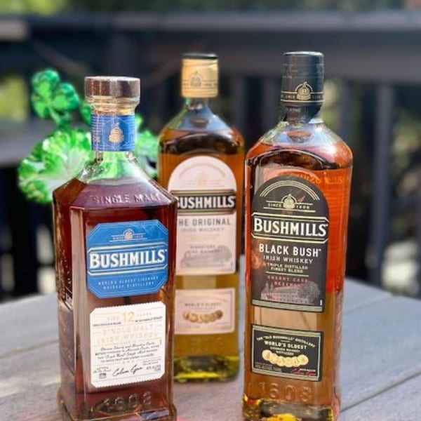 Three bottles of Bushmills Irish whiskey, including Single Malt and Black Bush, on a wooden surface.
