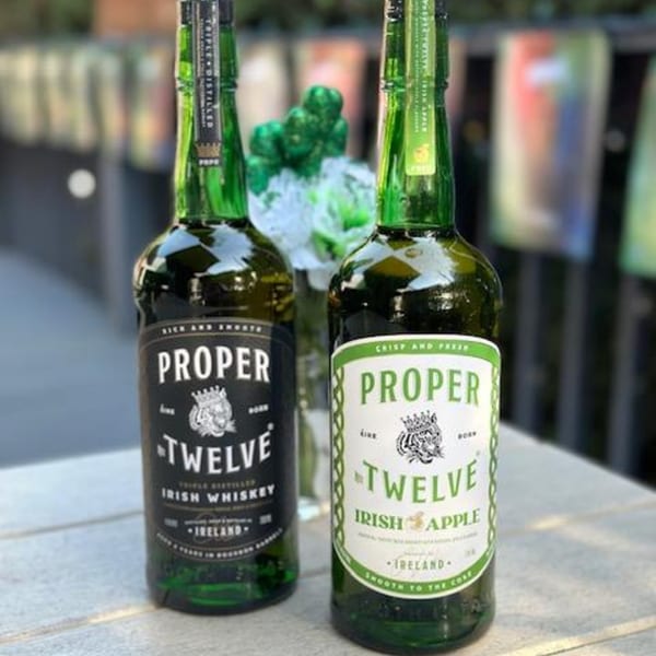 Two green bottles of Proper Twelve Irish Whiskey and Irish Apple on a table with green decorations.