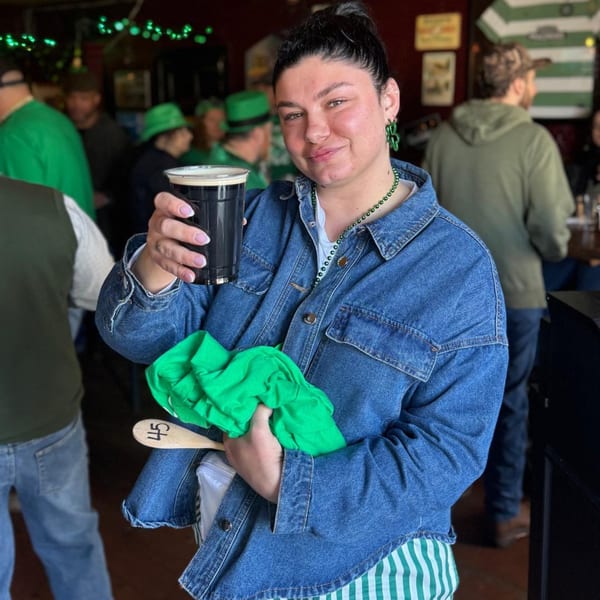 A woman in a denim jacket holds a dark beer and a green cloth at Trooper Thorn's Irish Beef House.