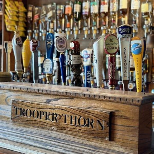 A wooden bar tap with "Trooper Thorn" carved into it, featuring various beer taps.