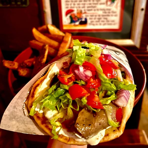 A gyro with meat, lettuce, tomatoes, and onions, served with a side of fries.