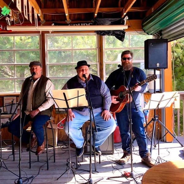Three men performing Irish music on a sunny outdoor patio stage at Trooper Thorn's.