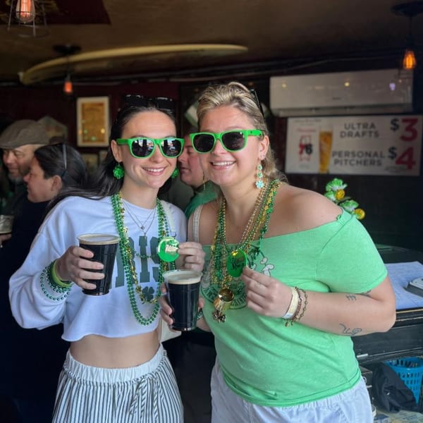 Two women in green sunglasses and St. Patrick's Day beads hold dark beers at Trooper Thorn's Irish Beef House.