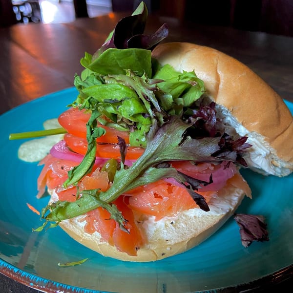 A bagel with cream cheese, smoked salmon, red onion, tomato, and mixed greens on a blue plate.