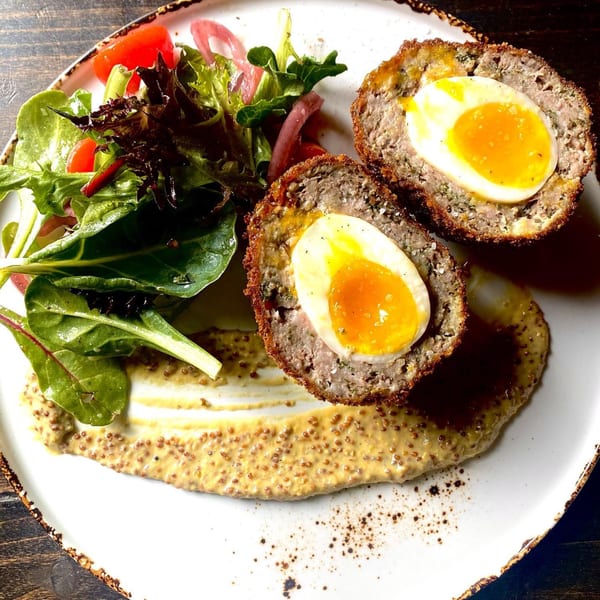 Two halved Scotch eggs with runny yolks, served with a side salad and whole grain mustard.