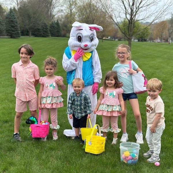 Children with Easter baskets pose with the Easter Bunny on a grassy lawn.