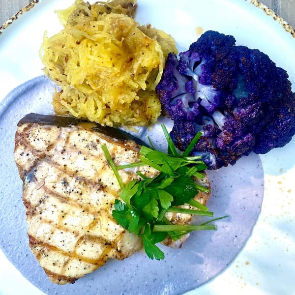 Grilled fish with spaghetti squash, purple cauliflower, and fresh herbs on a white plate.