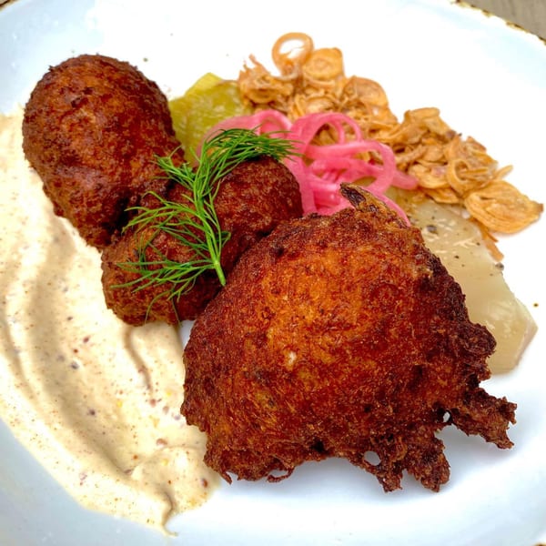 Three golden-brown Irish potato cakes with dill, pickled onions, and a creamy sauce on a white plate.